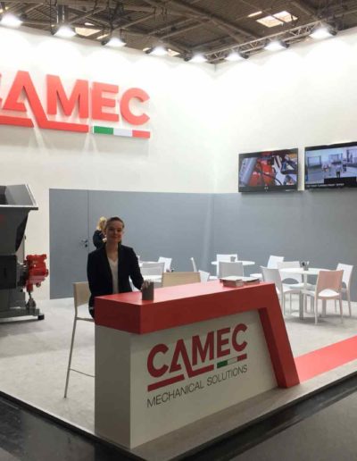 Messestand von Camec mit Logo, Empfangstresen, Maschinenprototyp, Bildschirme, Tische, Stühle.