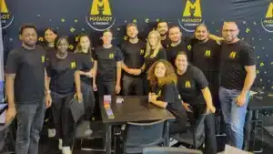 Gruppe von zwölf Personen in Matagot-T-Shirts vor Matagot & Friends Wand mit Kartentisch.